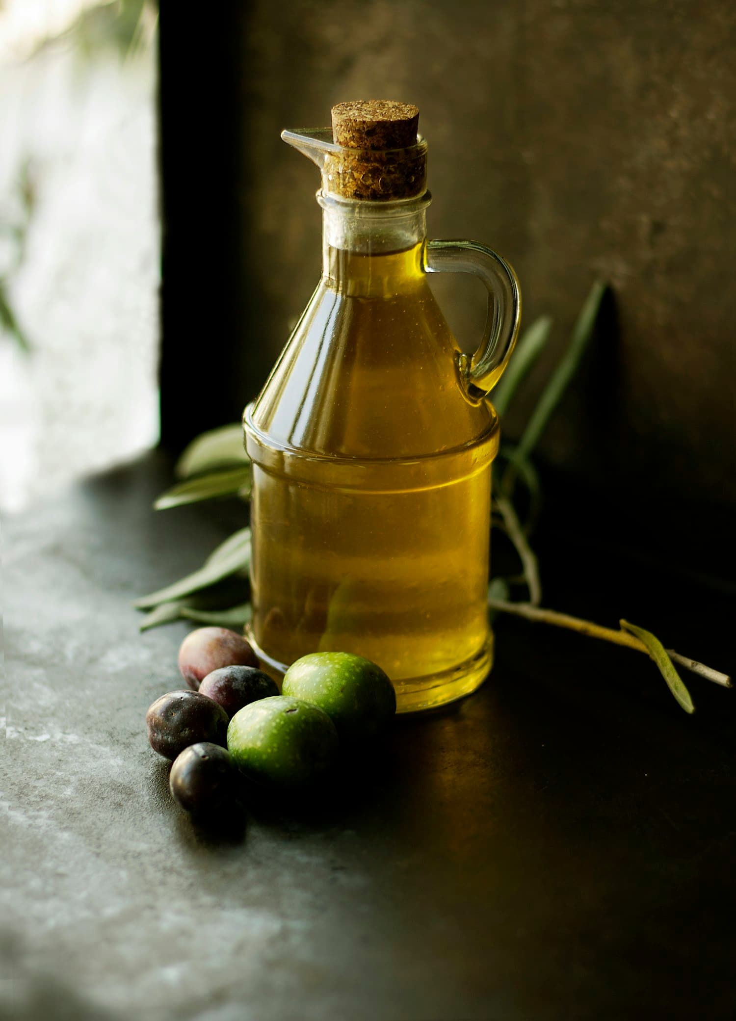 A bottle of golden cold-pressed oil beside fresh olives